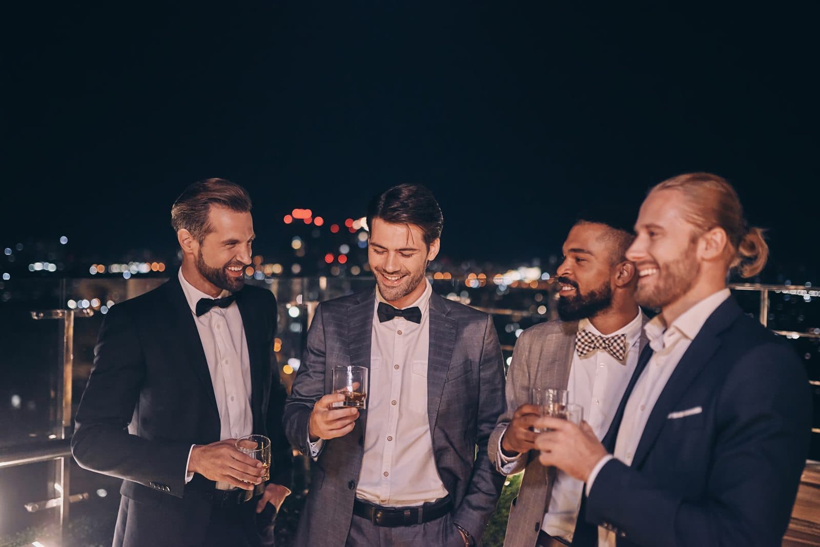 A group of friends in black tie sharing drinks on a rooftop at night
